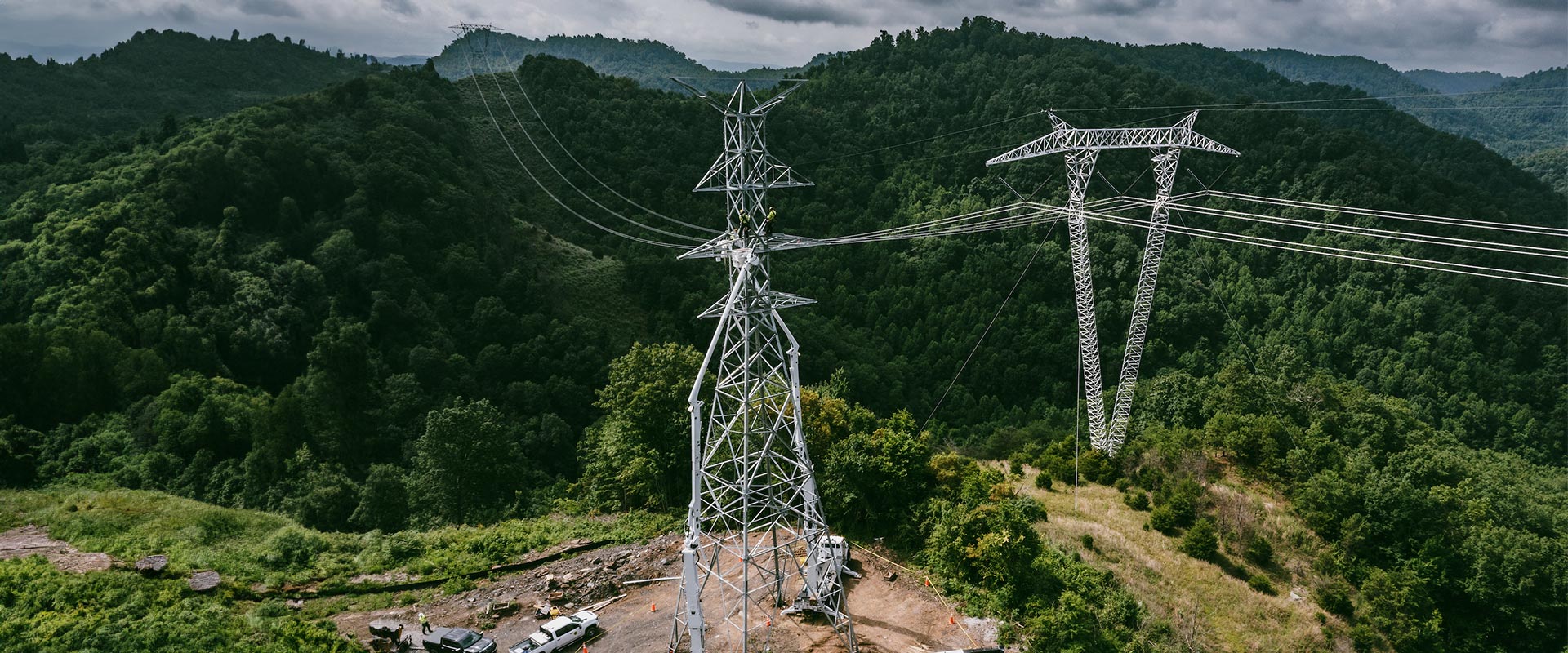 Aerial shot of steel electrical towers and power lines amid rolling hills of green forest