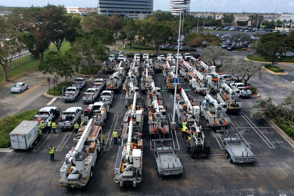 Aerial shot of a parking lot full of electrician's work vehicles and workers in yellow safety vests